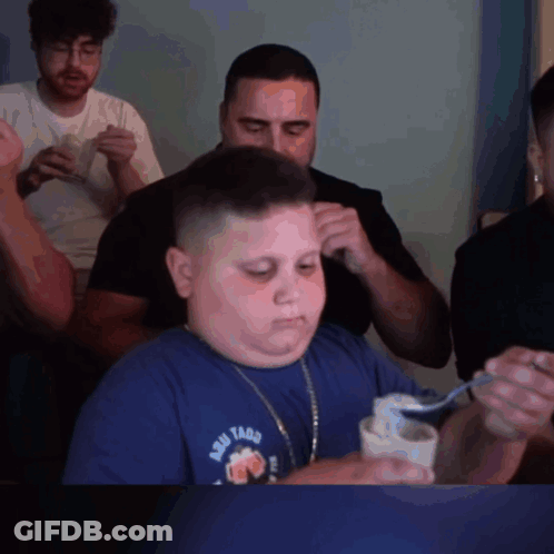 A Boy Wearing A Shirt That Says Aqui Tacos Is Eating Something With A Spoon GIF