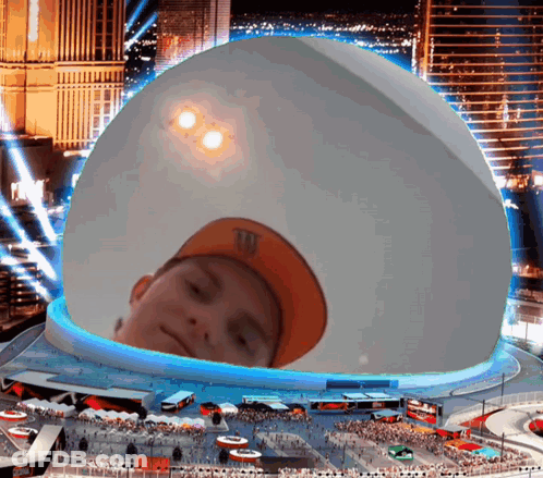 A Boy Wearing An Orange M & M 'S Hat Is Looking Out Of A Giant Dome GIF