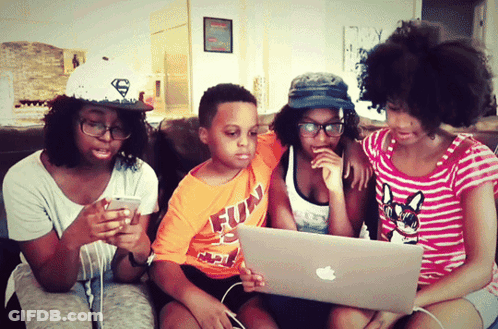 A Boy Wearing An Orange Shirt That Says Fun Is Looking At A Laptop GIF