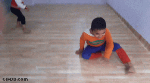 A Boy Wearing An Orange Shirt That Says ' Spiderman ' On It Is Doing A Handstand On The Floor GIF