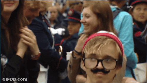 A Boy Wearing Glasses And A Fake Mustache Stands In A Crowd Of People With The Letters Nrk On The Bottom Right GIF