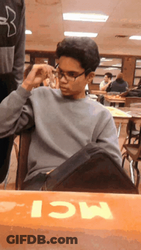 A Boy Wearing Glasses Sits At A Table With The Word Mci Written On It GIF