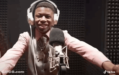 A Boy Wearing Headphones And A Pink Shirt Is Standing In Front Of A Microphone . GIF
