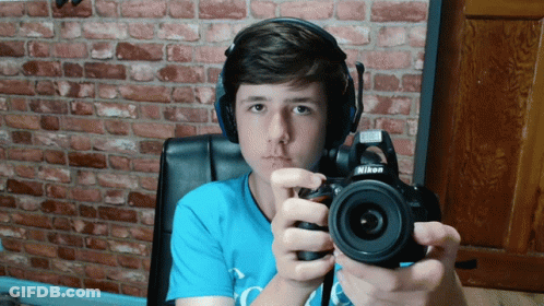 A Boy Wearing Headphones Holds A Nikon Camera In His Hands GIF