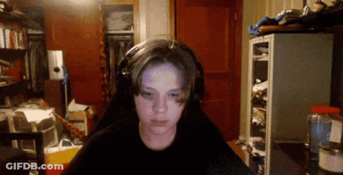 A Boy Wearing Headphones Looks At The Camera In A Cluttered Room GIF