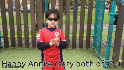 A Boy Wearing Sunglasses Stands In Front Of A Wooden Fence With The Words Happy Anniversary Both Of You GIF