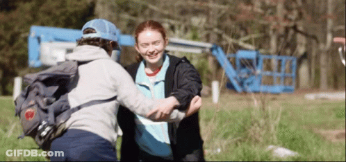 A Boy With A Backpack Is Hugging A Girl In A Field . GIF