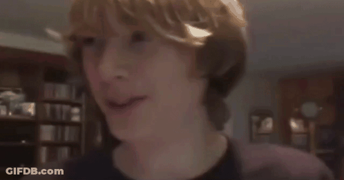 A Boy With Blonde Hair Is Smiling In A Dark Room GIF