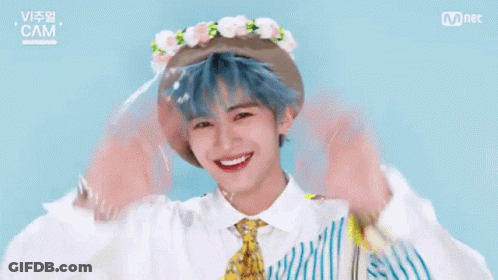 A Boy With Blue Hair And A Flower Crown On His Head Is Waving His Hands . GIF