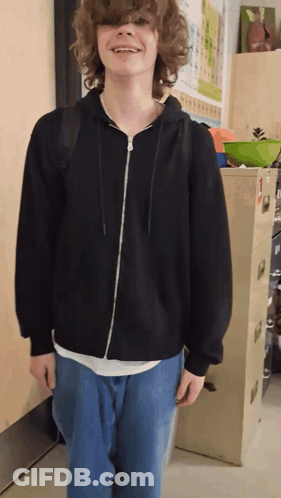 A Boy With Curly Hair Wearing A Black Hoodie And Jeans GIF