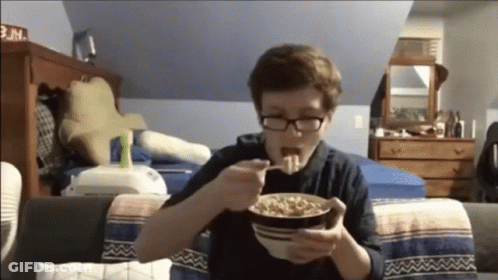 A Boy With Glasses Is Eating Cereal In A Bedroom GIF