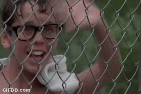 A Boy With Glasses Is Standing Behind A Chain Link Fence . GIF