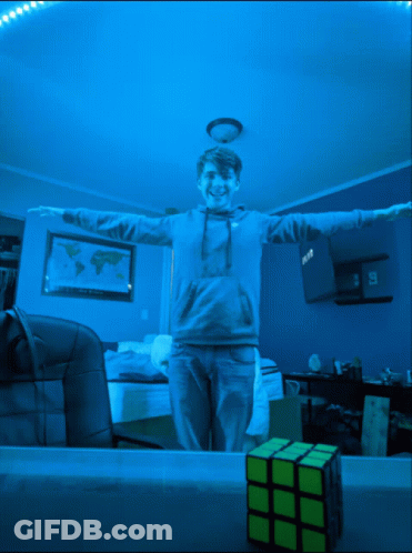 A Boy With His Arms Outstretched Is Standing Next To A Yellow Rubik 'S Cube GIF