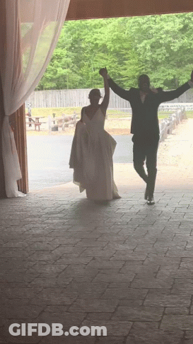 A Bride And Groom Are Dancing In A Barn With Their Arms Outstretched GIF