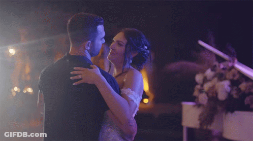 A Bride And Groom Are Dancing In Front Of A Piano In A Dark Room GIF