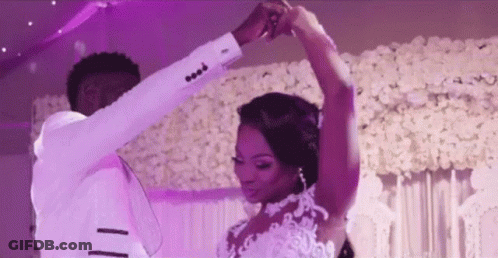 A Bride And Groom Are Dancing Together At Their Wedding Reception In Front Of A Wall Of Flowers . GIF