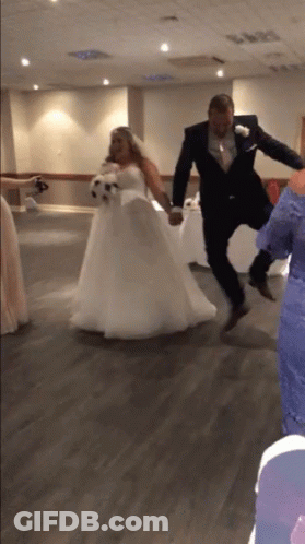 A Bride And Groom Are Jumping In The Air Holding Hands GIF