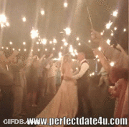 A Bride And Groom Are Kissing Under Sparklers At A Wedding GIF