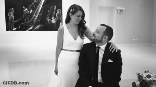 A Bride And Groom Are Posing For A Picture In Front Of An Exit Sign . GIF