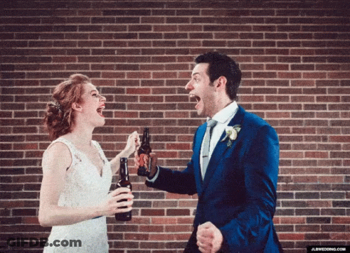 A Bride And Groom Are Toasting With Beer Bottles In Front Of A Brick Wall GIF