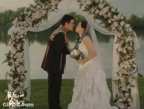 A Bride And Groom Kiss Under A Floral Arch With The Words Mother Gino 'S On The Bottom GIF