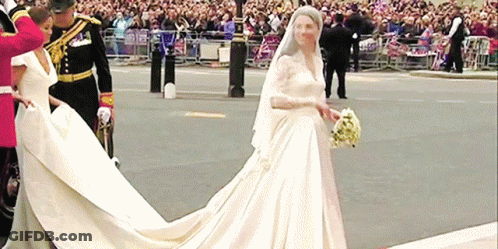 A Bride In A Long White Dress Is Walking Down A Street GIF