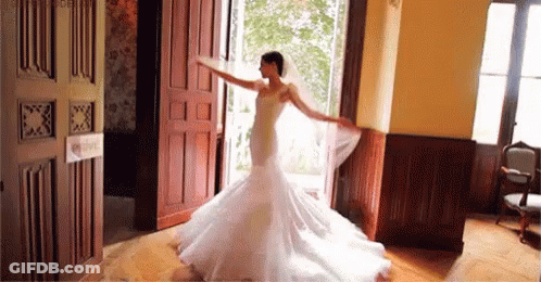 A Bride In A Wedding Dress And Veil Is Dancing In A Room . GIF