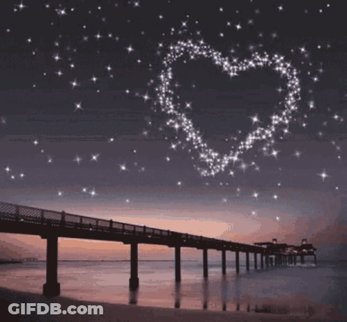 A Bridge Over A Body Of Water With A Heart Made Of Stars Above It GIF
