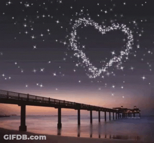 A Bridge Over A Body Of Water With A Heart Made Of Stars In The Sky GIF