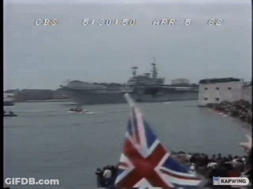 A British Flag Is Flying In Front Of A Large Ship On The Water GIF
