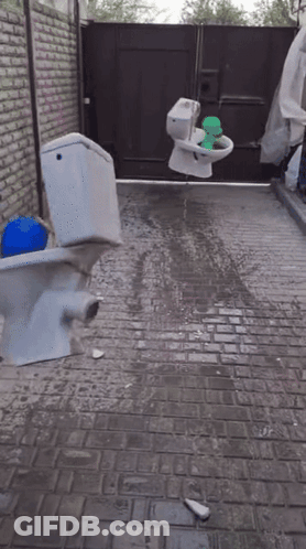 A Broken Toilet Sits On A Brick Sidewalk GIF