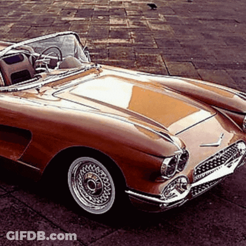 A Brown Sports Car With A Convertible Top Is Parked On The Side Of The Road GIF