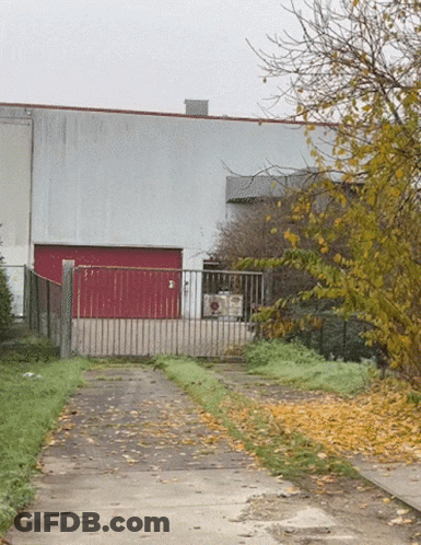 A Building With A Red Garage Door Is Behind A Gate GIF