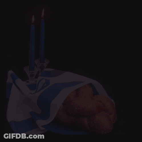 A Bunch Of Bread Is Wrapped In A Blue And White Cloth Next To Two Lit Candles GIF
