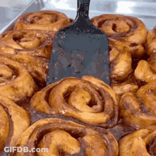 A Bunch Of Cinnamon Rolls With A Spatula In The Middle GIF