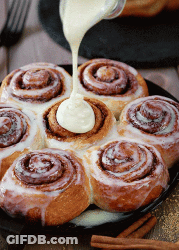 A Bunch Of Cinnamon Rolls With Frosting Being Poured On Them GIF