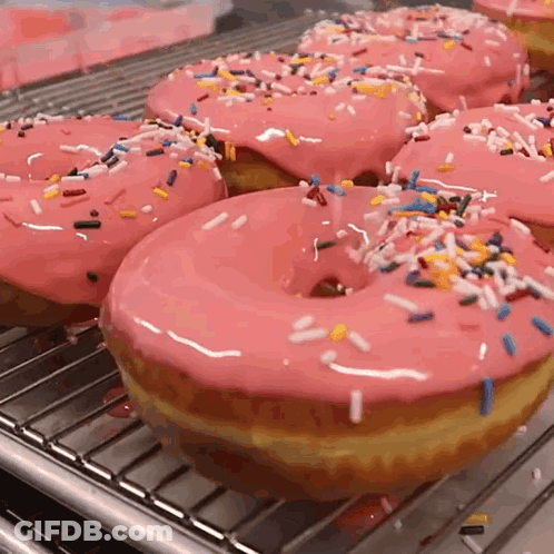 A Bunch Of Donuts With Pink Frosting And Sprinkles On A Rack GIF