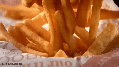 A Bunch Of French Fries Are Being Poured Out Of A Container GIF