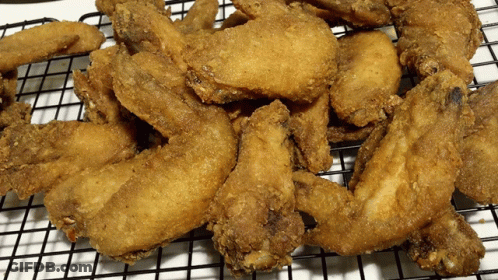 A Bunch Of Fried Chicken Wings Are Sitting On A Wire Rack GIF