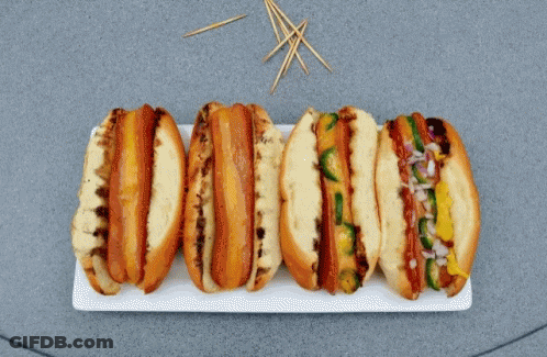A Bunch Of Hot Dogs On A Plate With Toothpicks In The Background GIF