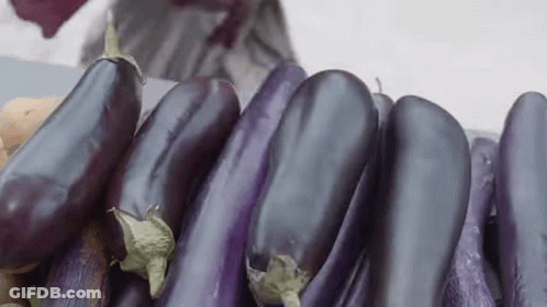 A Bunch Of Purple Eggplants Are Sitting On Top Of A Table . GIF