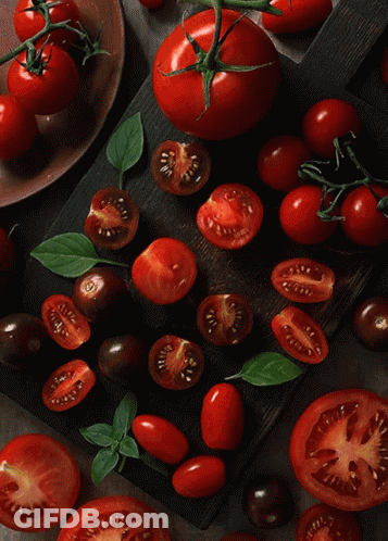 A Bunch Of Sliced Tomatoes Are On A Wooden Cutting Board GIF