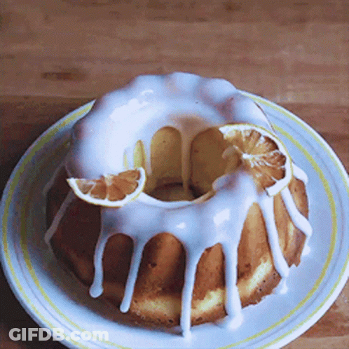 A Bundt Cake With White Frosting And Slices Of Orange On A White Plate GIF