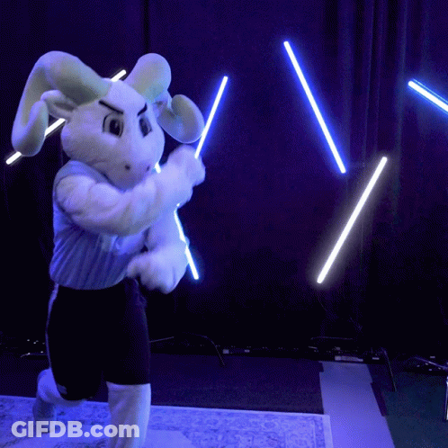 A Bunny Mascot Is Holding Two Lightsabers In Front Of A Blue Curtain GIF
