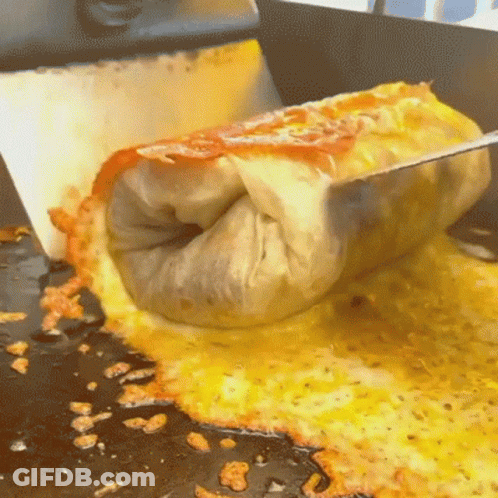 A Burrito Is Being Cut In Half On A Stove Top GIF