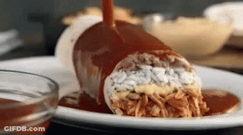 A Burrito On A Plate With Sauce Being Poured On It . GIF