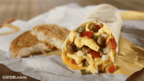 A Burrito With Eggs Sausage And Vegetables Is On A Piece Of Paper GIF