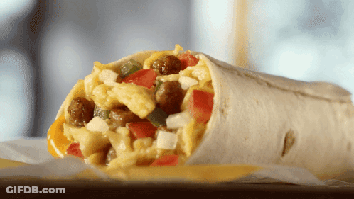 A Burrito With Scrambled Eggs Sausage Tomatoes And Cheese On A Table GIF