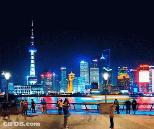 A Busy City At Night With A Sign That Says Aunow GIF