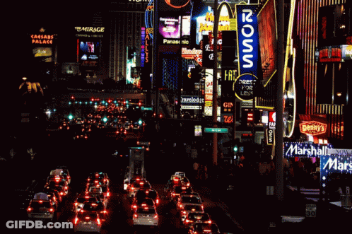 A Busy City Street At Night With A Mcdonald 'S Sign In The Foreground GIF